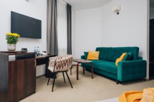 zielona kanapa z pomarańczowymi poduszkami, obok stolik kawowy i biurko