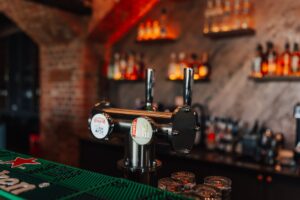 zbliżenie na dystrybutor piwa, w tle butelki z alkoholem